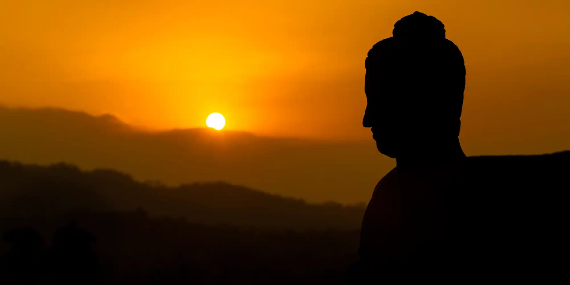 Silhouette d'une statue de Bouddha contre un ciel orange.